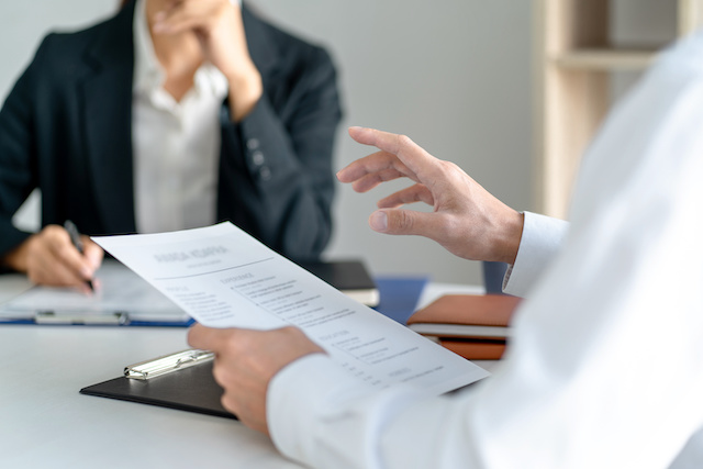 A male hiring manager interviews a female candidate while reviewing her resume.