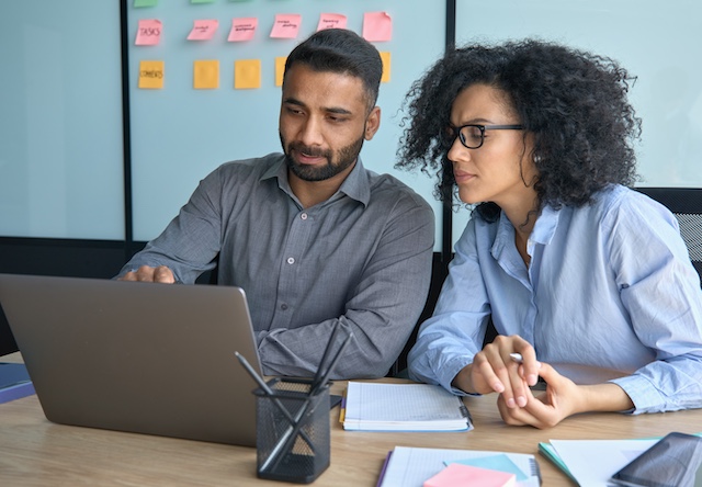 A female employee gets feedback from her male manager working on a laptop