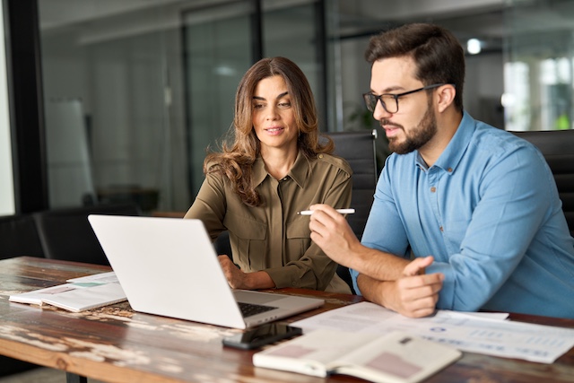 A female manager mentors a male employee on a project working at a laptop