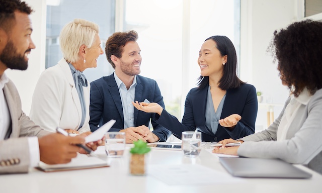 A young Asian female manager shares her enthusiasm with her diverse team at a meeting