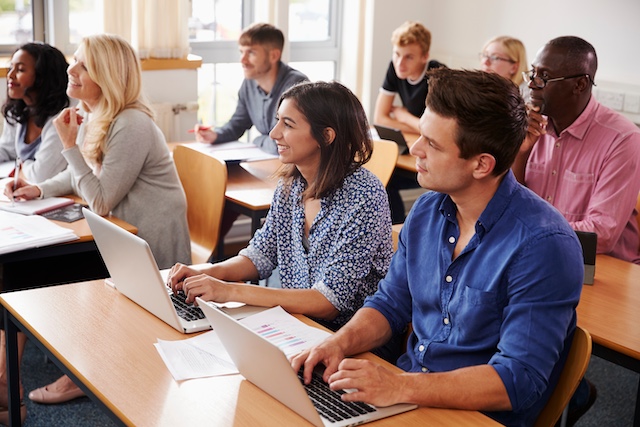 Adults attend a class, sitting at desks with their laptops