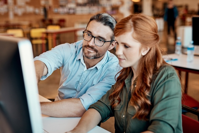 A manager helps his female employee at her desk
