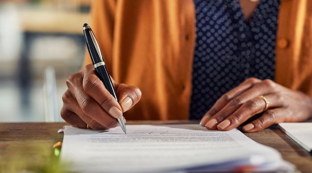 A Black woman signs an agreement.