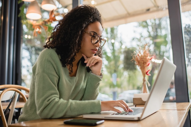 African American woman concentrates while reading something on her laptop at home.