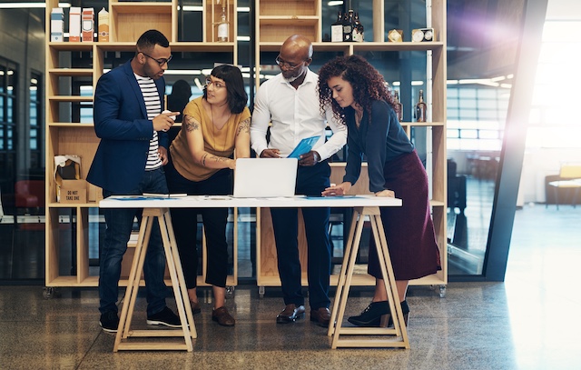 Coworkers brainstorm while standing around a laptop in an office