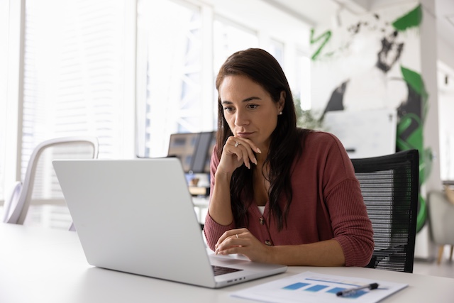 A businesswoman looks thoughtfully at her computer at work